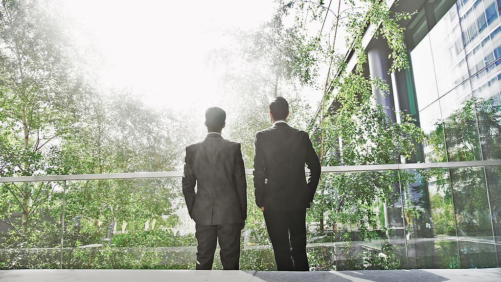 Two business men standing in green office building looking at the sun