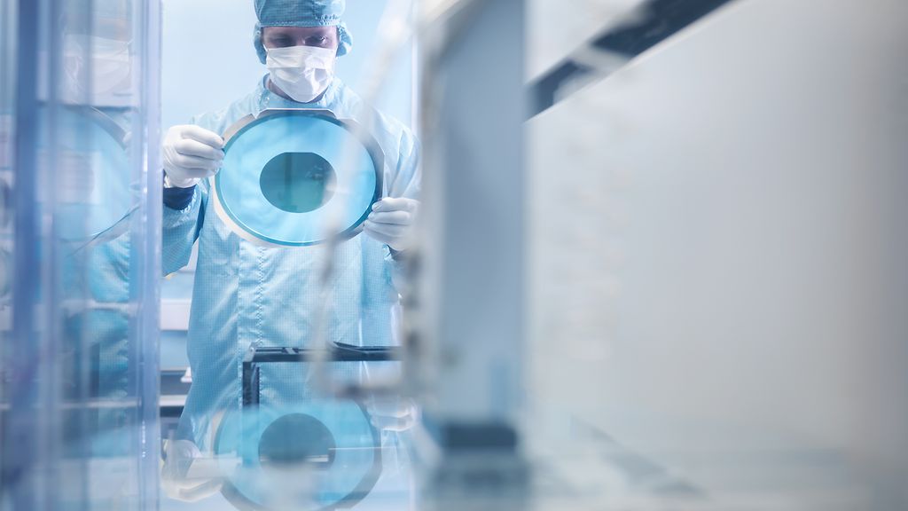 Elektronikerin beim Halten von Siliziumwafern durch Schneidemaschine im Reinraum